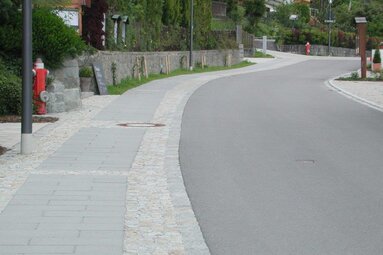 Das Bild zeigt eine neu geteerte Straße und einen Gehweg aus Granitsteinen. Am linken Bildrand ist eine Granitmauer vor einer Hecke zu sehen.  | © Markt Bodenmais